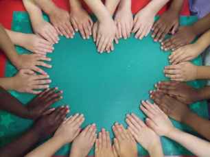 People of different backgrounds placing their hands together to form a heart.